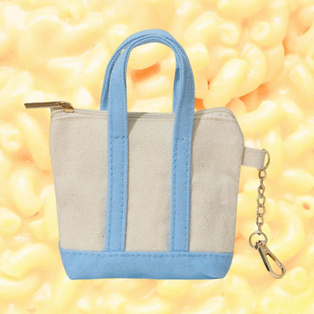 A small canvas tote-style keychain with light blue handles, trim, and base, plus a gold-tone zipper and keychain clasp, shown against a yellow macaroni-patterned background.