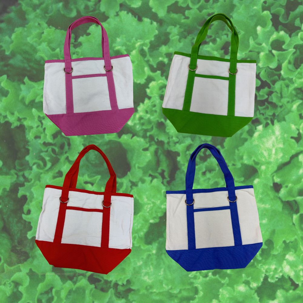 Four canvas tote bags arranged in a 2x2 grid, each with a white front pocket and a contrasting bottom and handle color: pink, green, red, and blue. The bags are set against a green lettuce background.